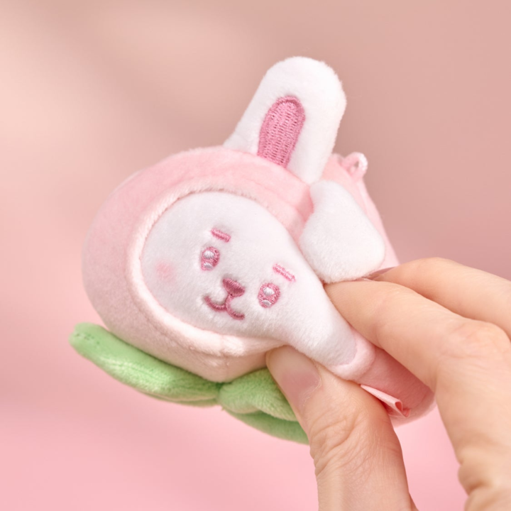 BT21 Peach Holic COOKY stress ball being gently squeezed by hand on a pink background