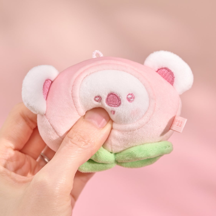 BT21 Peach Holic KOYA stress ball being gently squeezed by hand on a pink background