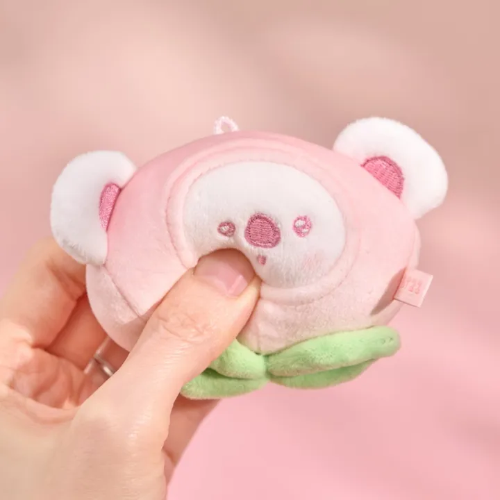 BT21 Peach Holic KOYA stress ball being gently squeezed by hand on a pink background