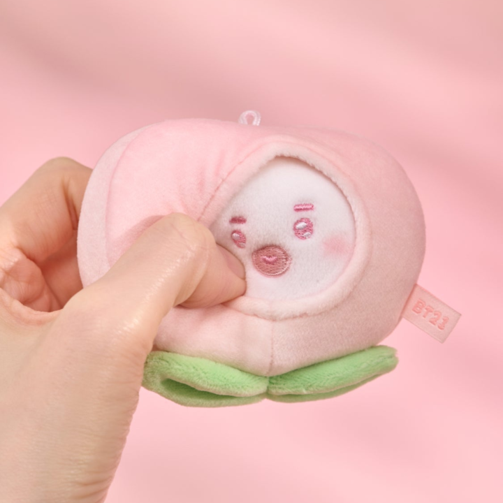 BT21 Peach Holic TATA stress ball being gently squeezed by hand on a pink background